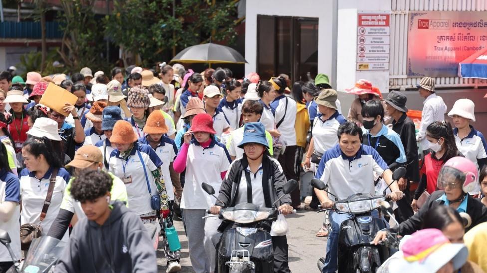 A large group of workers are leaving Trax Apparel, some on motorbikes.