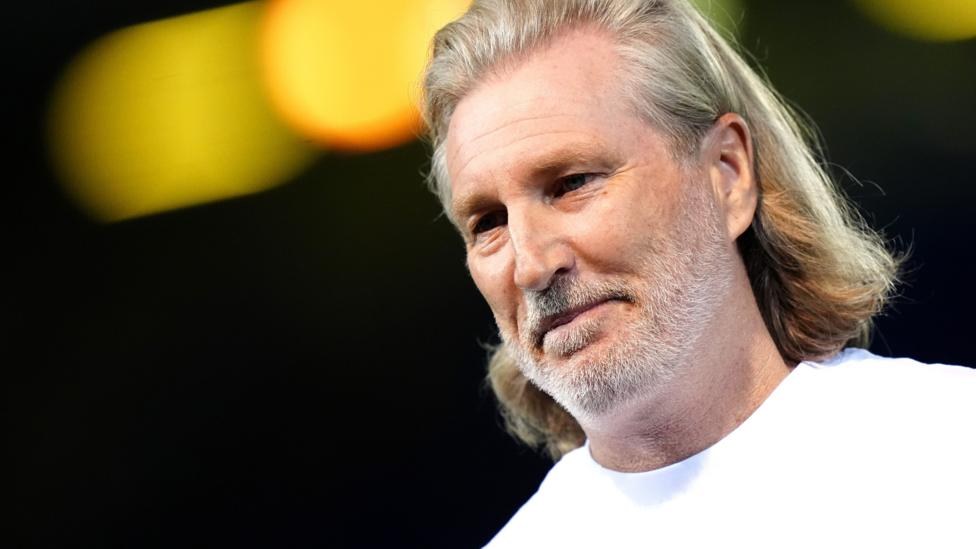 Robbie Savage in a white t-shirt watching Peterborough against Ipswich Under-21s from the touchline